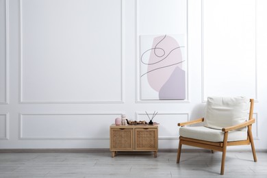 Photo of Comfortable beige armchair and wooden cabinet with decor near white wall indoors, space for text
