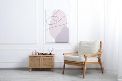 Photo of Comfortable beige armchair and wooden cabinet with decor near white wall indoors