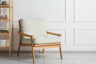 Photo of Comfortable beige armchair and wooden shelving unit with decor near white wall indoors, space for text