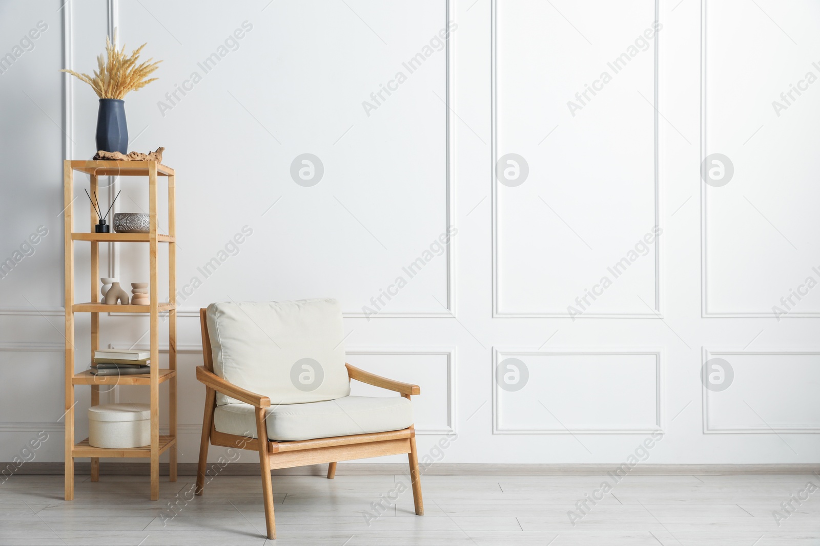 Comfortable beige armchair and wooden shelving unit with decor near white wall indoors, space for text Photo of Comfortable beige armchair and wooden shelving unit with decor near white wall indoors, space for text