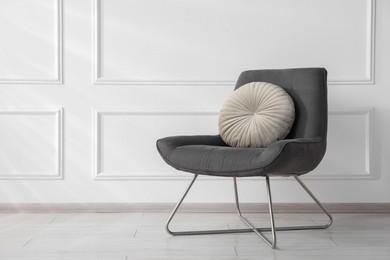 Photo of Comfortable armchair with cushion near white wall indoors, space for text