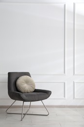 Photo of Comfortable armchair with cushions near white wall indoors, space for text