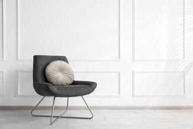 Photo of Comfortable armchair with cushions near white wall indoors, space for text