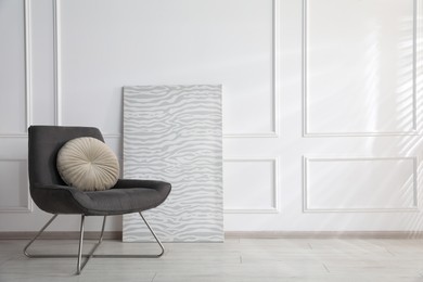 Photo of Comfortable armchair with cushions near white wall indoors, space for text