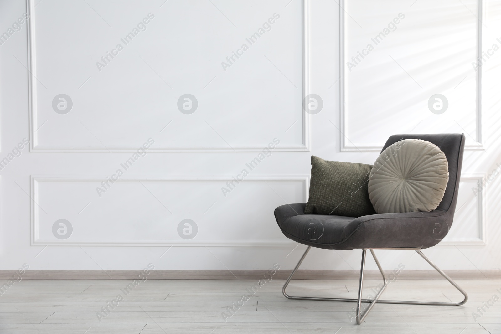 Comfortable armchair with cushions near white wall indoors, space for text Photo of Comfortable armchair with cushions near white wall indoors, space for text