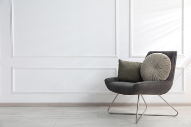Photo of Comfortable armchair with cushions near white wall indoors, space for text