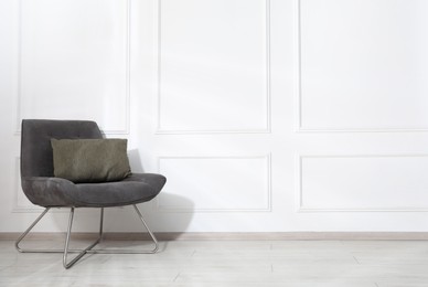 Photo of Comfortable armchair with cushion near white wall indoors, space for text