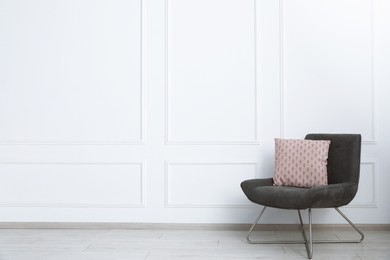 Photo of Comfortable armchair with cushion near white wall indoors, space for text