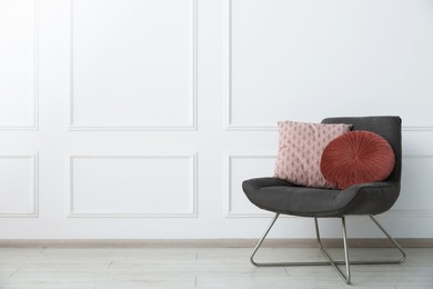 Photo of Comfortable armchair with cushions near white wall indoors, space for text