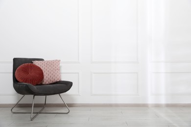 Photo of Comfortable armchair with cushions near white wall indoors, space for text