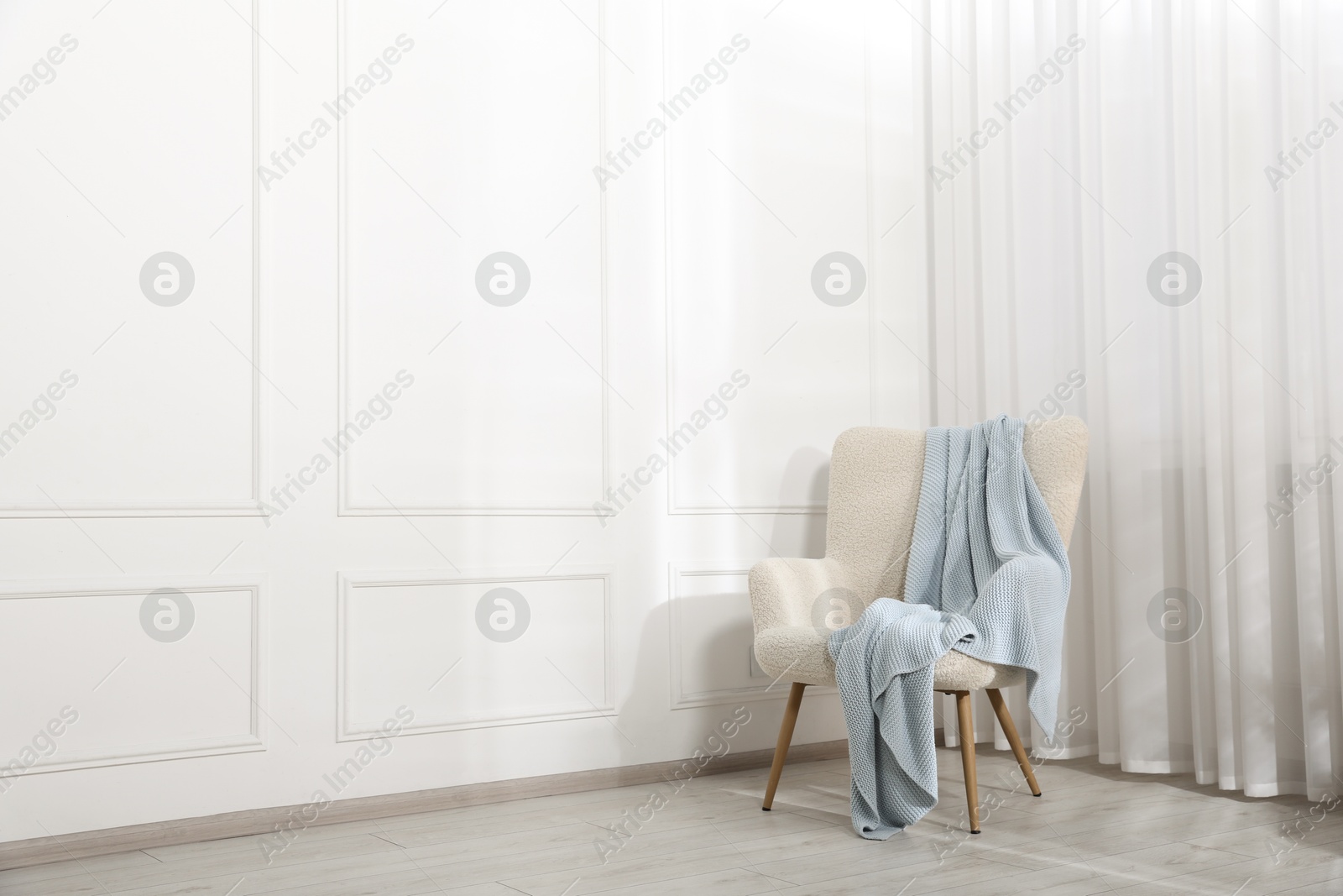 Comfortable armchair with blanket near white wall indoors, space for text Photo of Comfortable armchair with blanket near white wall indoors, space for text