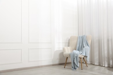 Photo of Comfortable armchair with blanket near white wall indoors, space for text
