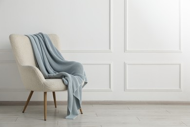 Photo of Comfortable armchair with blanket near white wall indoors, space for text