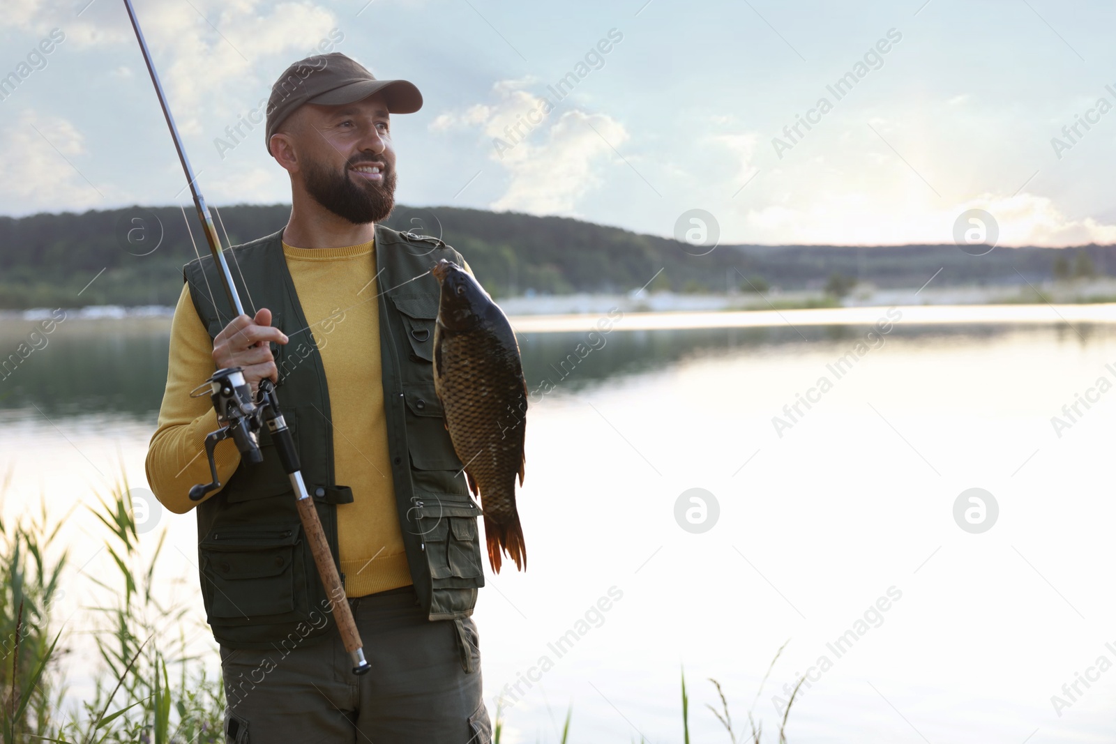 Smiling fisherman holding rod and caught fish near lake at summer. Space for text Photo of Smiling fisherman holding rod and caught fish near lake at summer. Space for text