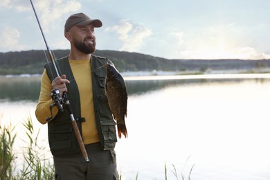 Photo of Smiling fisherman holding rod and caught fish near lake at summer. Space for text