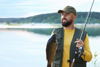 Photo of Smiling fisherman holding rod and caught fish near lake at summer. Space for text