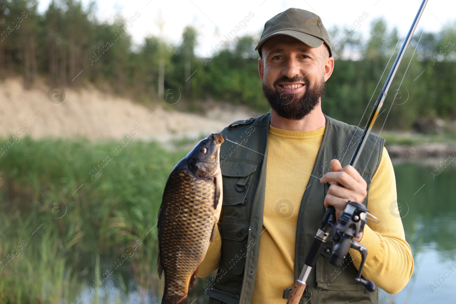 Smiling fisherman holding rod and caught fish near lake at summer Photo of Smiling fisherman holding rod and caught fish near lake at summer