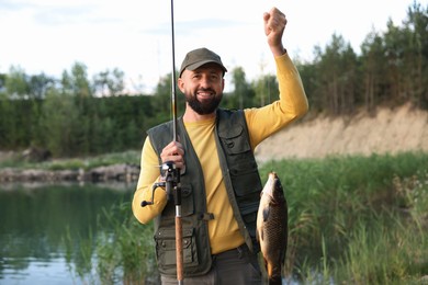 Photo of Smiling fisherman holding rod and caught fish near lake at summer