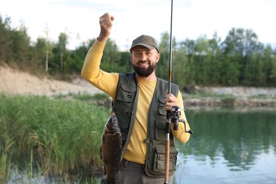 Photo of Smiling fisherman holding rod and caught fish near lake at summer