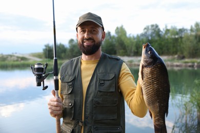 Photo of Smiling fisherman holding rod and caught fish near lake at summer