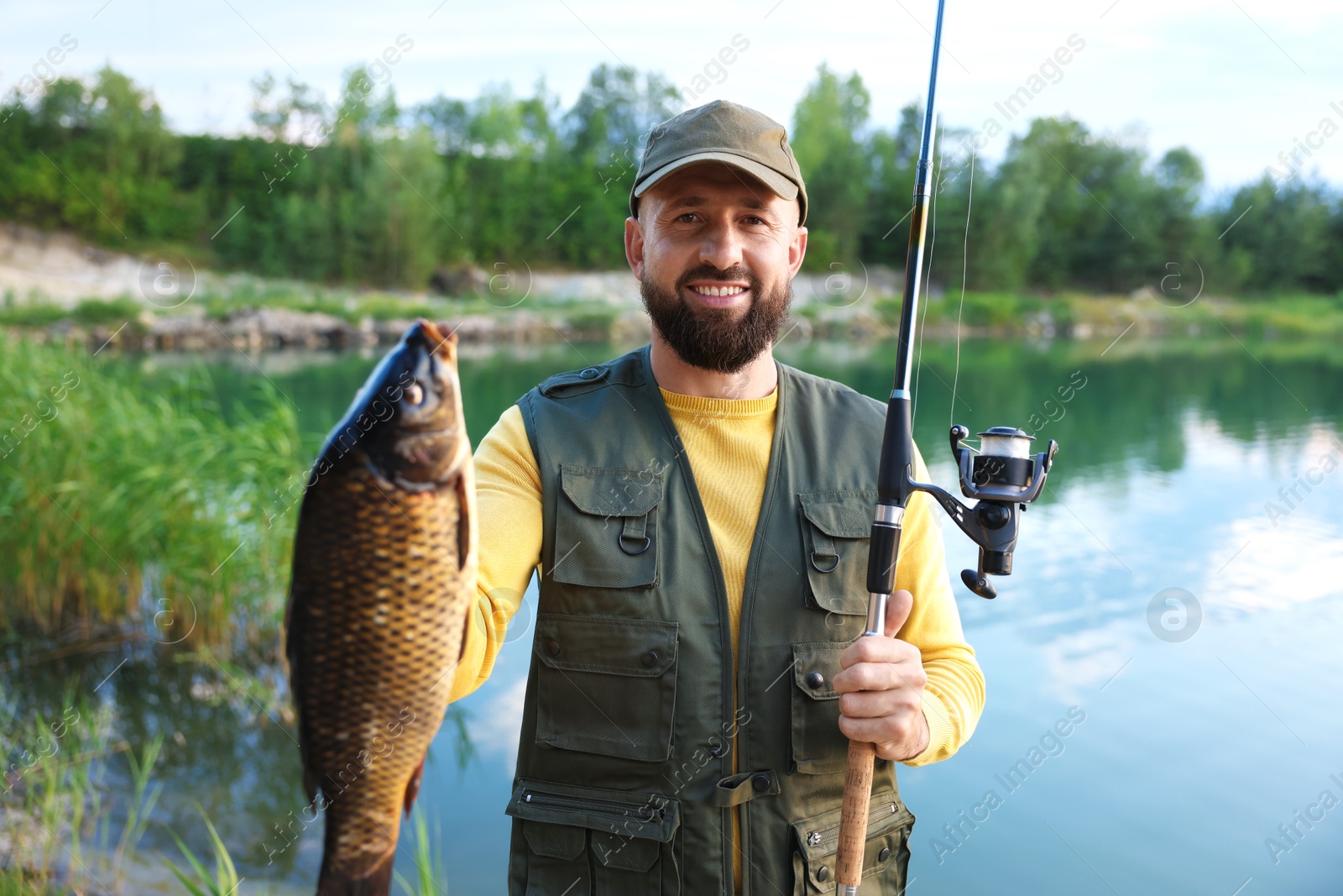 Smiling fisherman holding rod and caught fish near lake at summer Photo of Smiling fisherman holding rod and caught fish near lake at summer