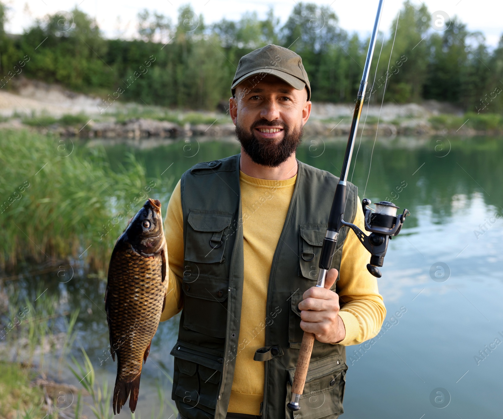 Smiling fisherman holding rod and caught fish near lake at summer Photo of Smiling fisherman holding rod and caught fish near lake at summer