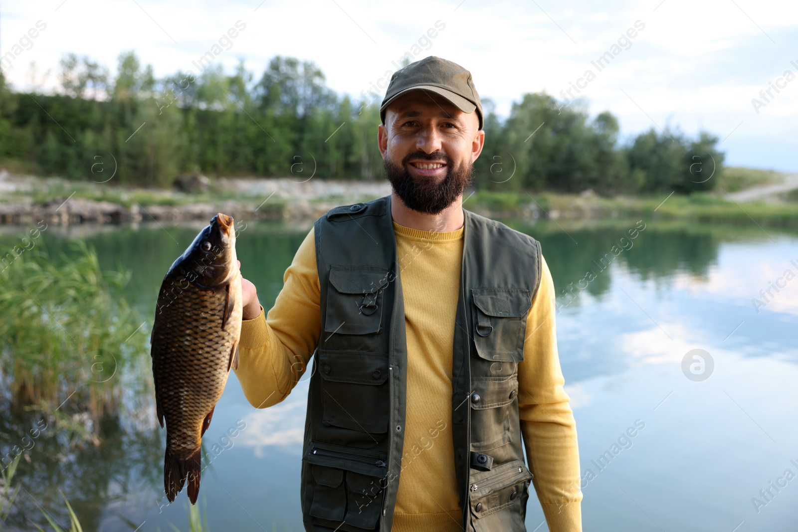 Smiling fisherman holding caught fish near lake at summer Photo of Smiling fisherman holding caught fish near lake at summer