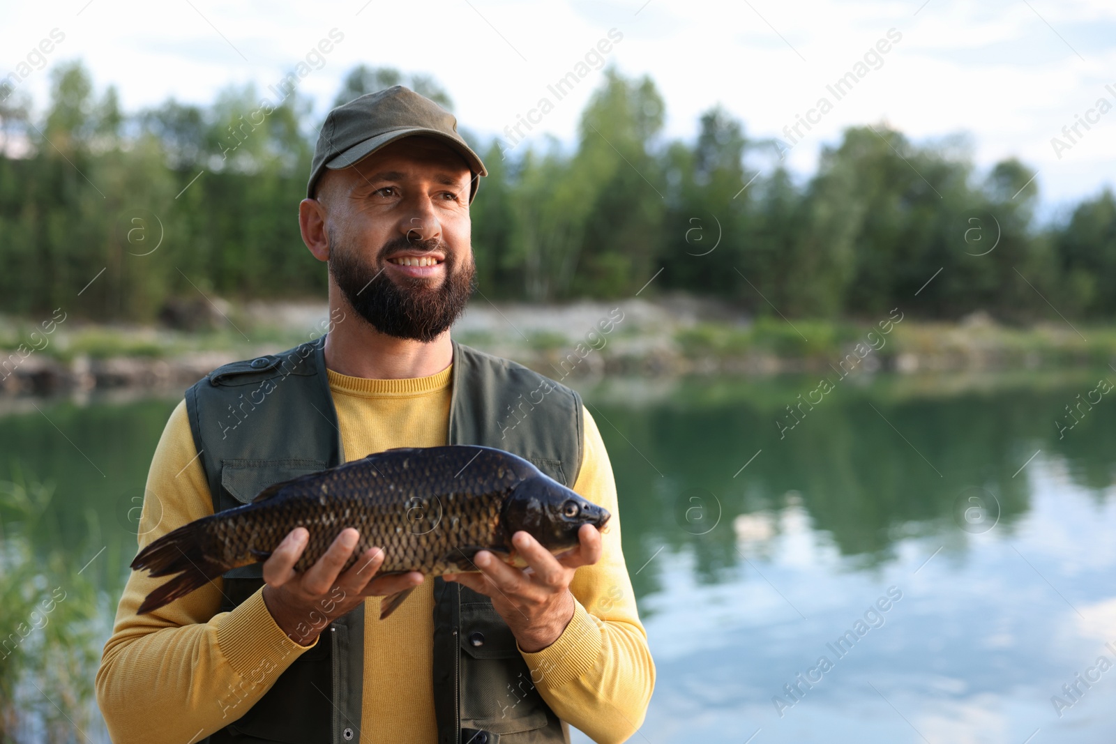 Smiling fisherman holding caught fish near lake at summer. Space for text Photo of Smiling fisherman holding caught fish near lake at summer. Space for text