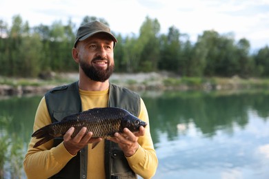 Photo of Smiling fisherman holding caught fish near lake at summer. Space for text