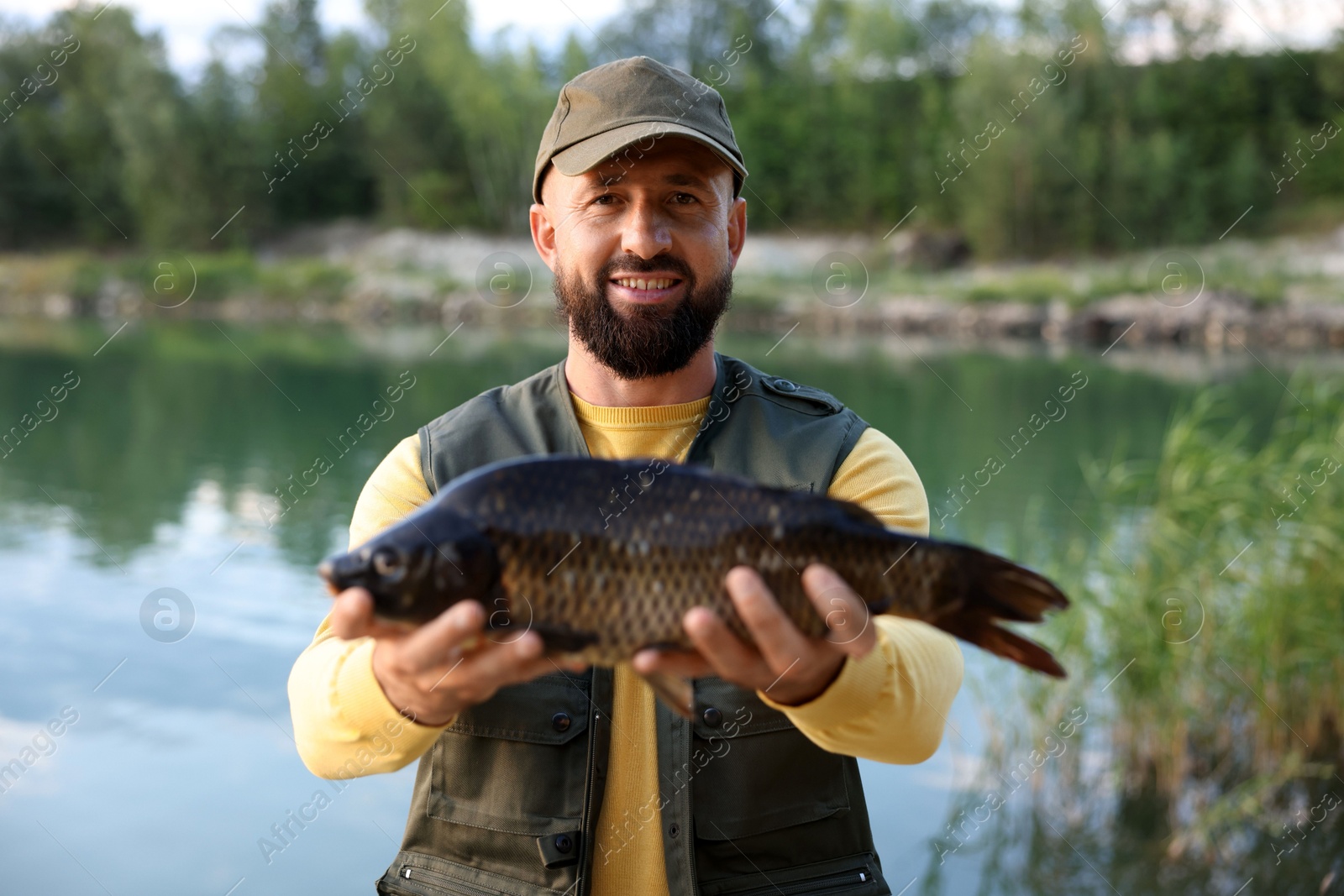 Smiling fisherman holding caught fish near lake at summer Photo of Smiling fisherman holding caught fish near lake at summer