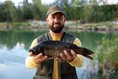 Photo of Smiling fisherman holding caught fish near lake at summer