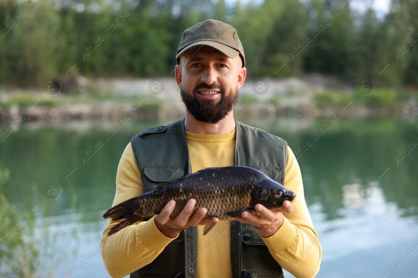 Smiling fisherman holding caught fish near lake at summer Photo of Smiling fisherman holding caught fish near lake at summer