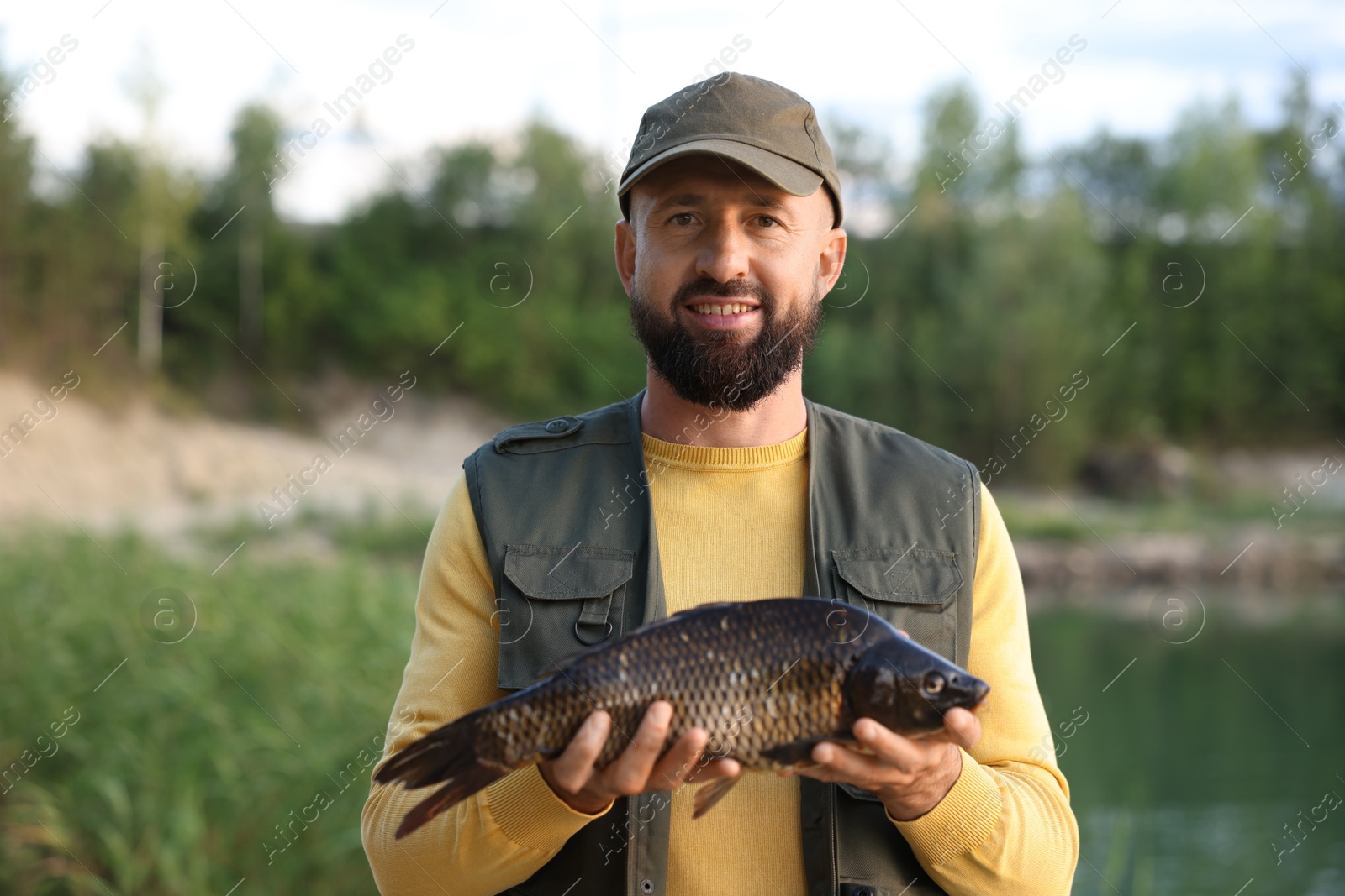 Smiling fisherman holding caught fish near lake at summer Photo of Smiling fisherman holding caught fish near lake at summer