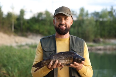 Photo of Smiling fisherman holding caught fish near lake at summer