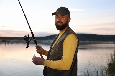 Photo of Fisherman with rod fishing near lake at sunset