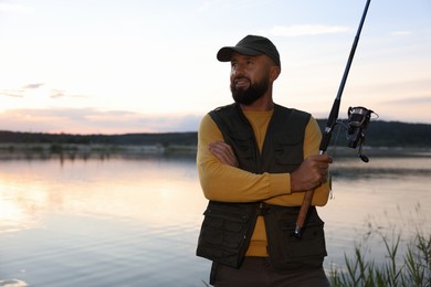 Photo of Fisherman with rod fishing near lake at sunset. Space for text