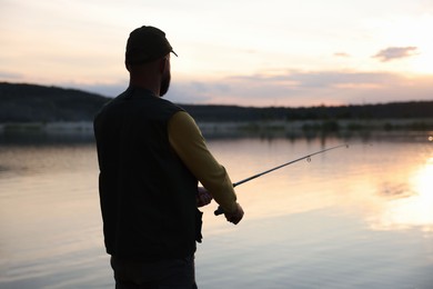 Photo of Fisherman with rod fishing near lake at sunset