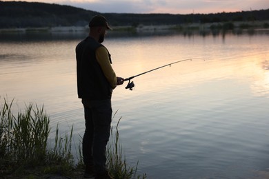 Photo of Fisherman with rod fishing near lake at sunset