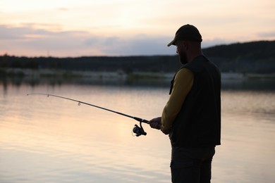 Photo of Fisherman with rod fishing near lake at sunset