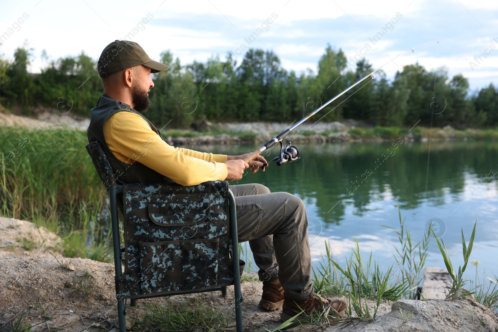 Fisherman with rod sitting on chair and fishing near lake at summer Photo of Fisherman with rod sitting on chair and fishing near lake at summer