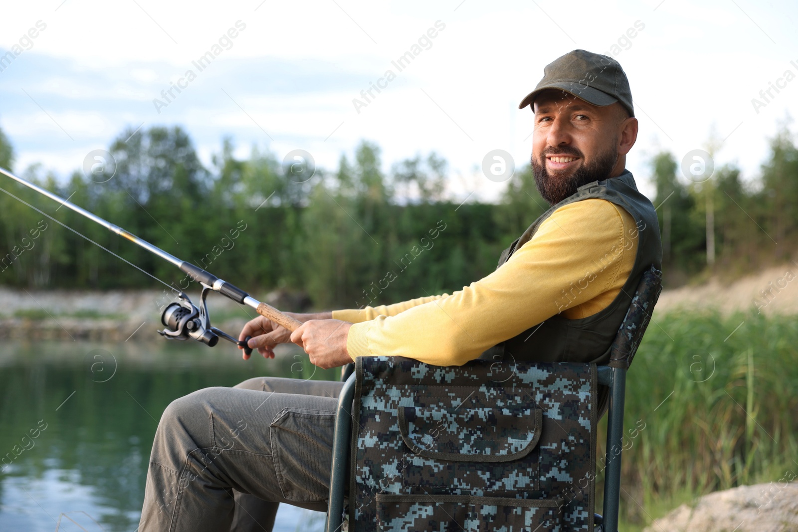 Fisherman with rod sitting on chair and fishing near lake at summer Photo of Fisherman with rod sitting on chair and fishing near lake at summer
