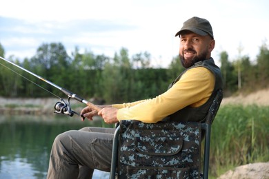 Photo of Fisherman with rod sitting on chair and fishing near lake at summer