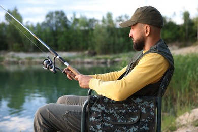 Photo of Fisherman with rod sitting on chair and fishing near lake at summer