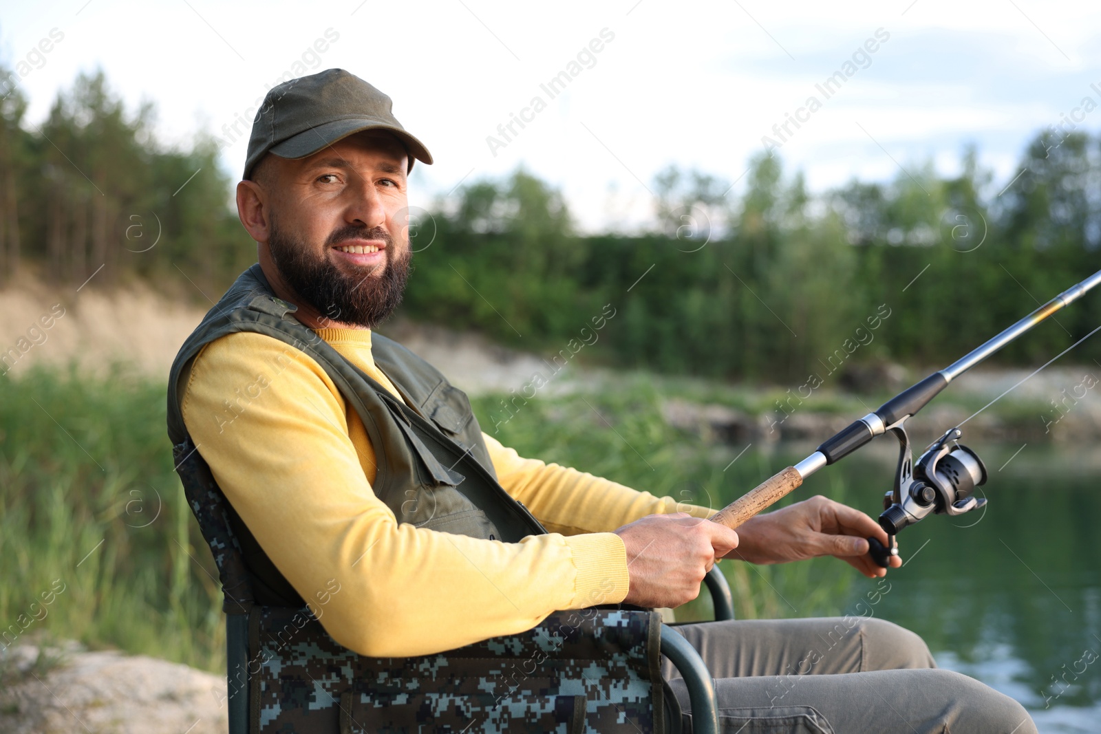 Fisherman with rod sitting on chair and fishing near lake at summer Photo of Fisherman with rod sitting on chair and fishing near lake at summer