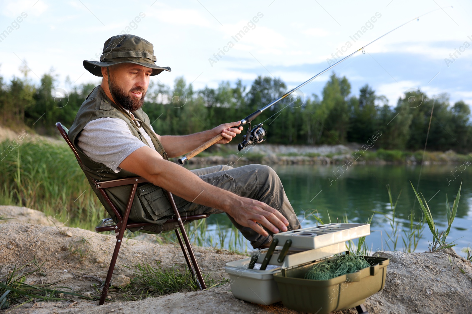 Fisherman with rod and other equipment fishing near lake at summer Photo of Fisherman with rod and other equipment fishing near lake at summer