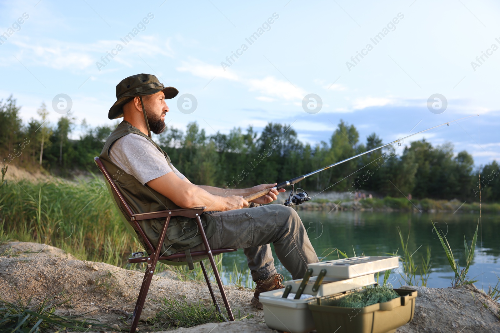 Fisherman with rod sitting on chair and fishing near lake at summer Photo of Fisherman with rod sitting on chair and fishing near lake at summer
