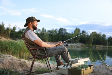 Photo of Fisherman with rod sitting on chair and fishing near lake at summer