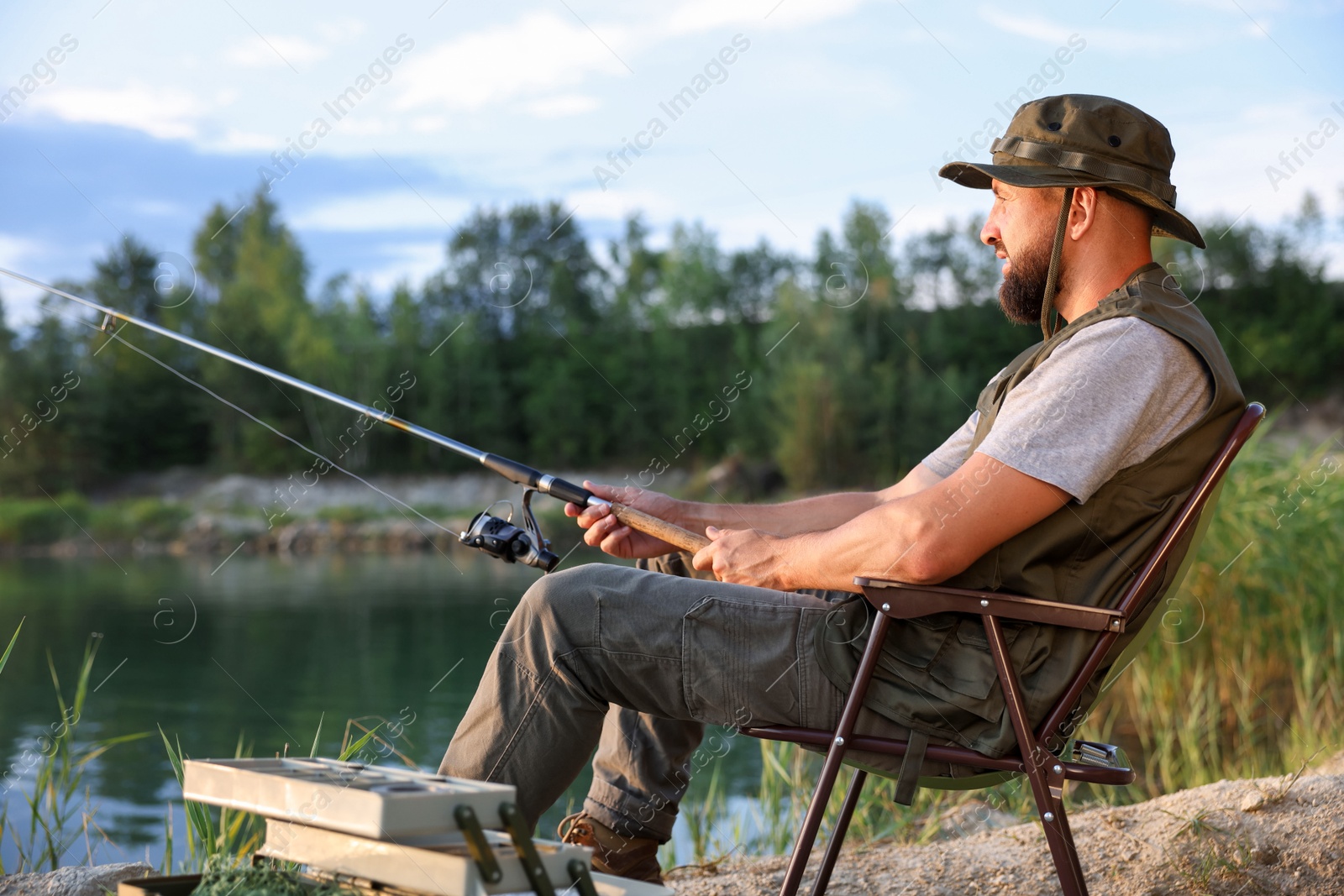 Fisherman with rod sitting on chair and fishing near lake at summer Photo of Fisherman with rod sitting on chair and fishing near lake at summer
