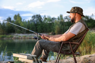 Photo of Fisherman with rod sitting on chair and fishing near lake at summer