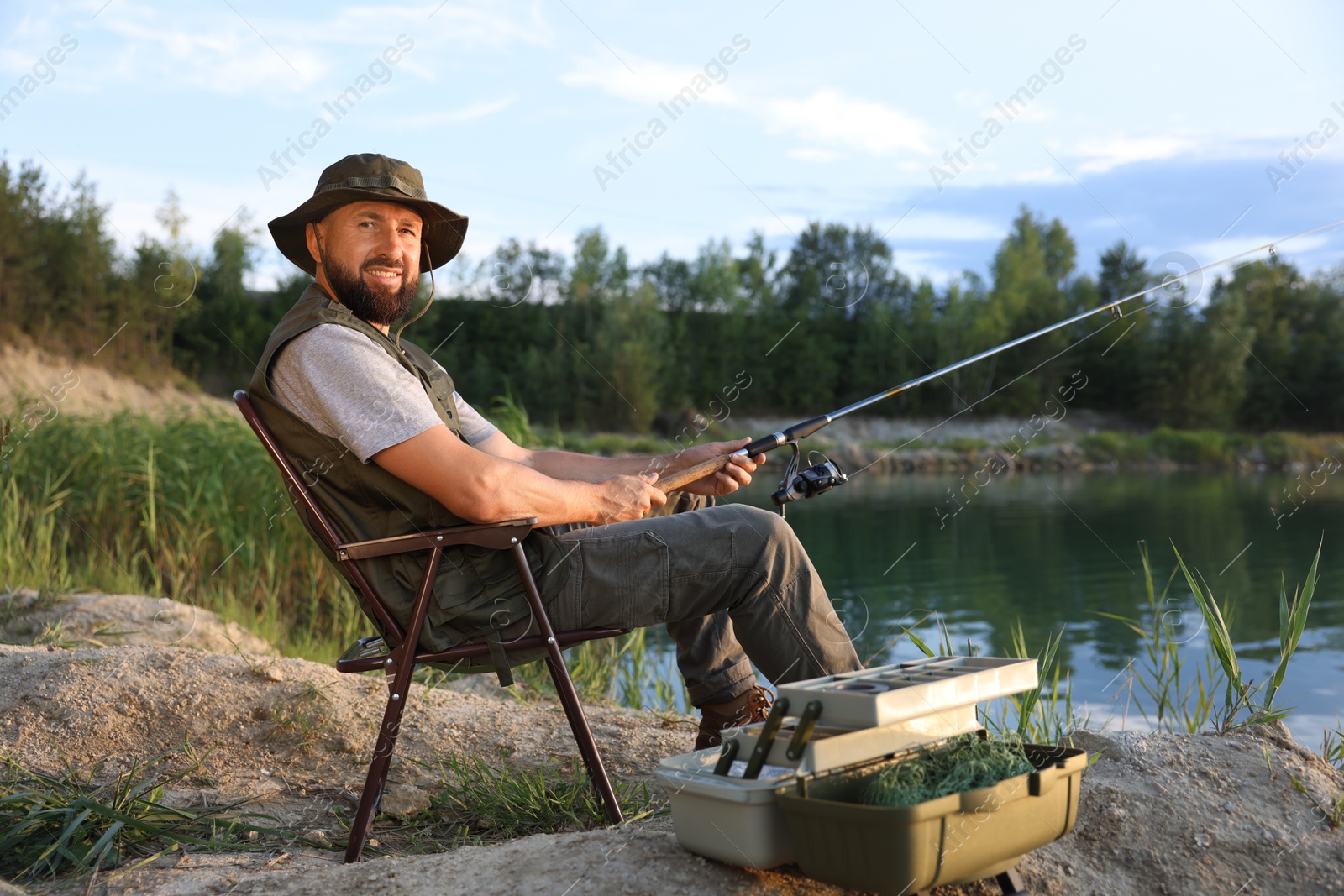 Fisherman with rod sitting on chair and fishing near lake at summer Photo of Fisherman with rod sitting on chair and fishing near lake at summer